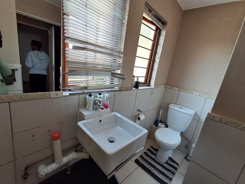 A compact bathroom featuring a wall-mounted basin, toilet, and tiled finishes. The space requires cosmetic updates and better concealment of exposed plumbing.