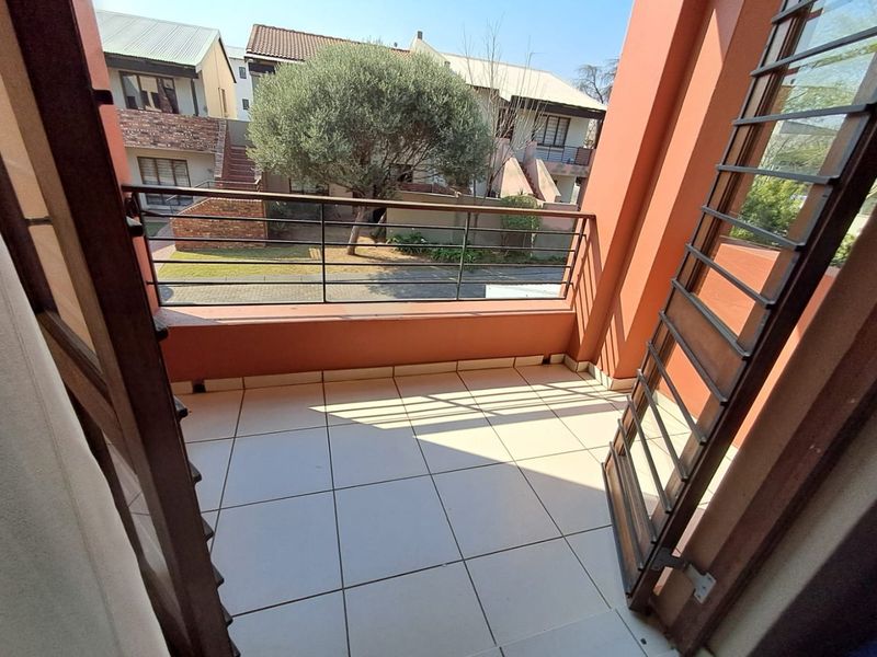 A clean, tiled balcony featuring a metal balustrade and security gate, offering an open view of the complex grounds.