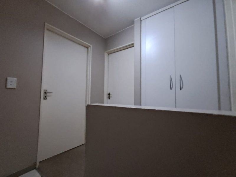 A clean, neutral hallway featuring built-in storage cupboards and access to adjacent rooms.