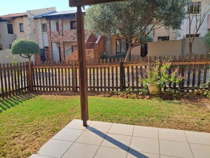 A private ground floor patio area featuring tiled flooring, a wooden pergola structure, and a small enclosed garden with a picket fence.