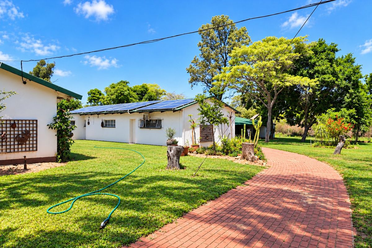 A well-maintained rear exterior view of the farm property featuring a brick paved walkway, lush green lawn, and roof-mounted solar panels.