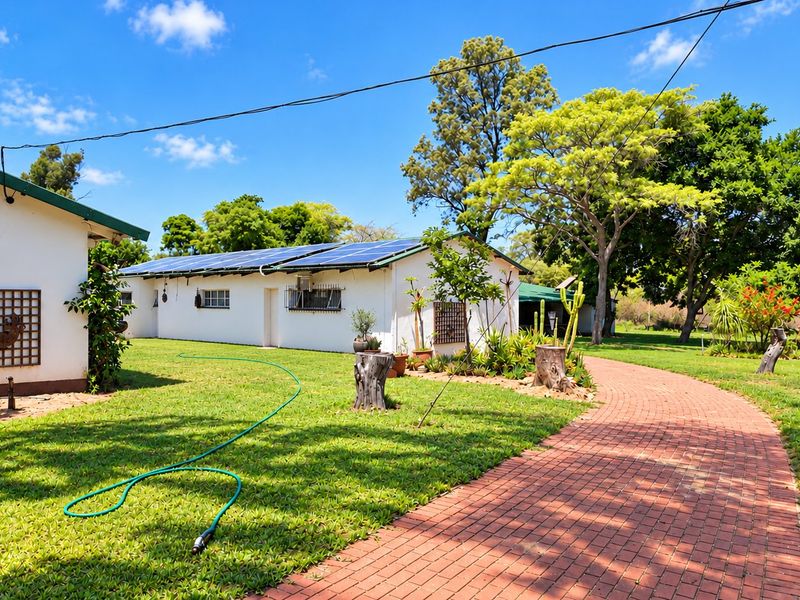 A well-maintained rear exterior view of the farm property featuring a brick paved walkway, lush green lawn, and roof-mounted solar panels.