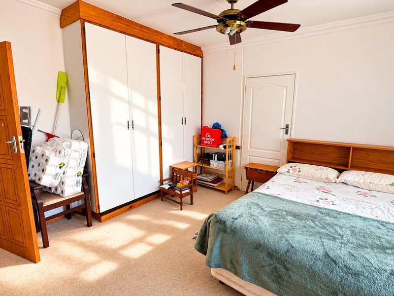 A well-lit bedroom featuring built-in cupboards, a ceiling fan, and carpeted flooring, offering a functional and comfortable living space.