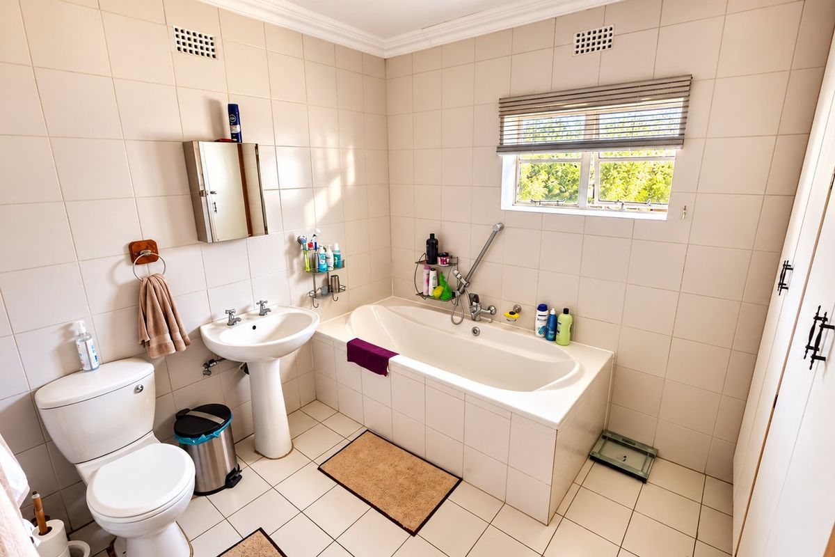 A functional bathroom featuring a pedestal basin, built-in bathtub, toilet, and tiled finishes, offering a clean and practical layout.