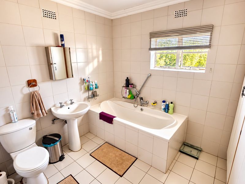 A functional bathroom featuring a pedestal basin, built-in bathtub, toilet, and tiled finishes, offering a clean and practical layout.