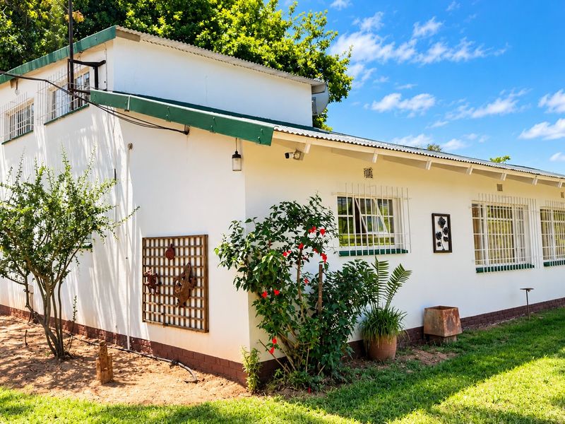 Rear view of the farm dwelling featuring a corrugated metal roof, security-barred windows, and a well-maintained lawn area.