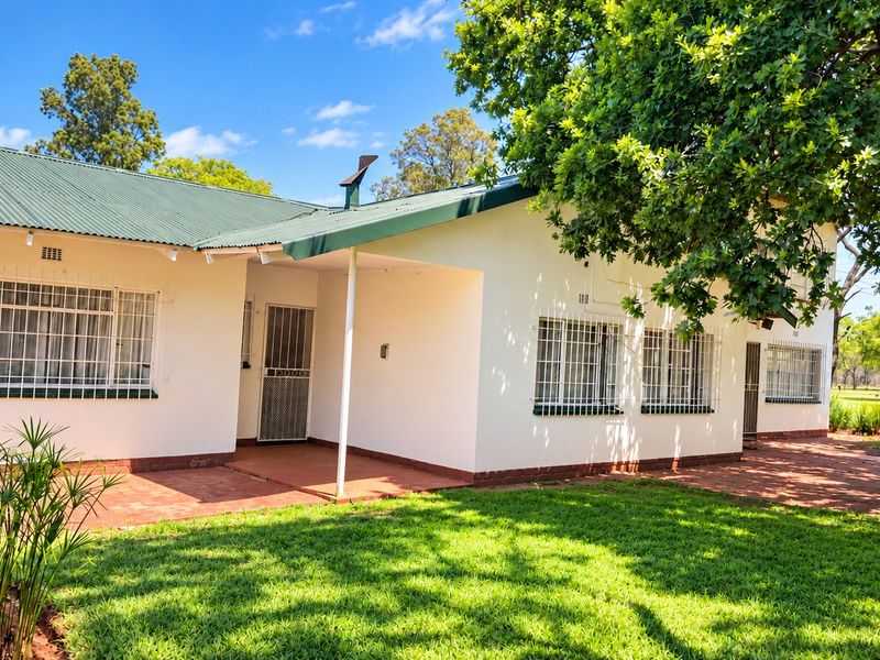 Rear view of the farmhouse featuring a covered patio, corrugated metal roof, and security-fitted windows overlooking a well-maintained garden.