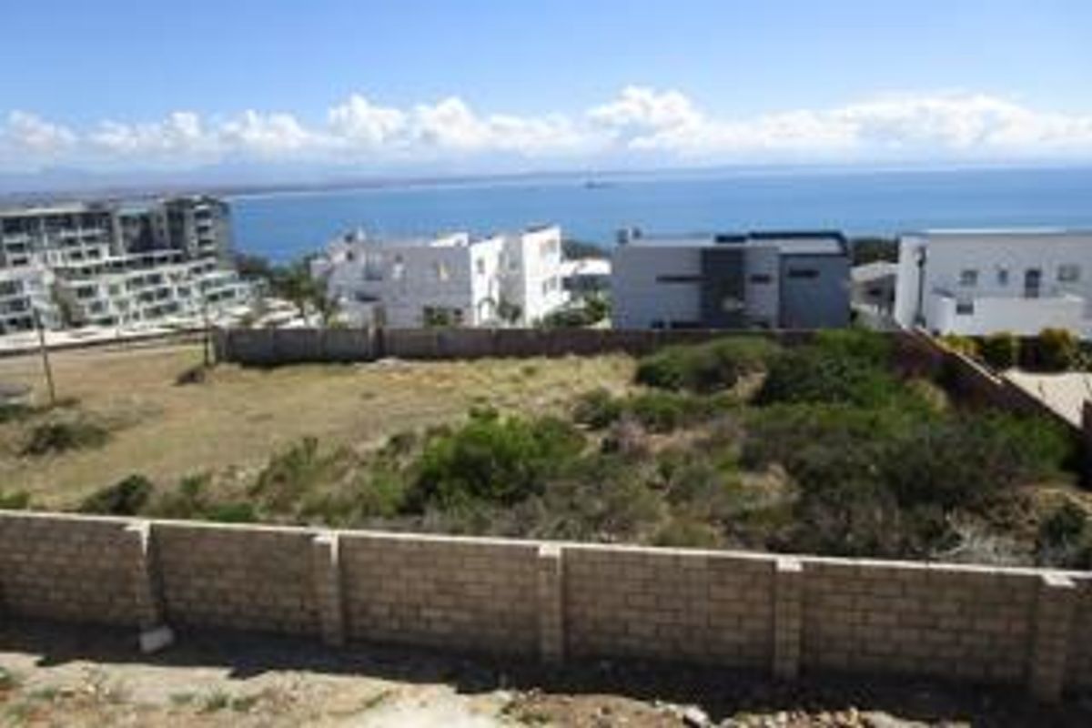 Vacant residential land plot featuring a clear coastal view and established boundary walling, situated in a developed neighborhood.