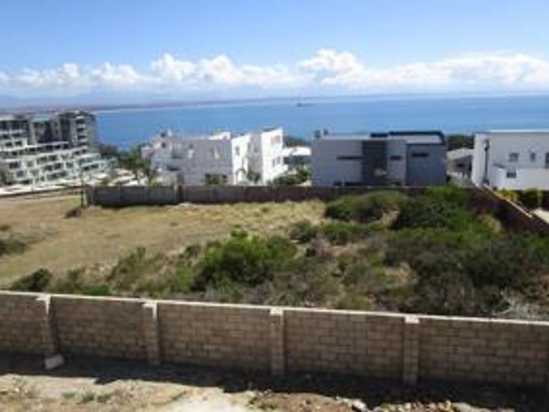 Vacant residential land plot featuring a clear coastal view and established boundary walling, situated in a developed neighborhood.