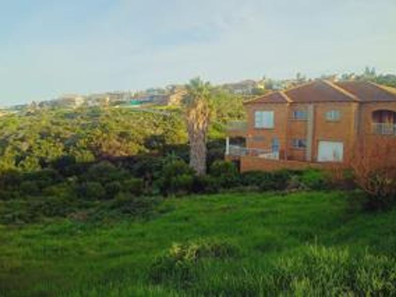 A view of the rear elevation of a brick residential property set within a sloped, grassy landscape.