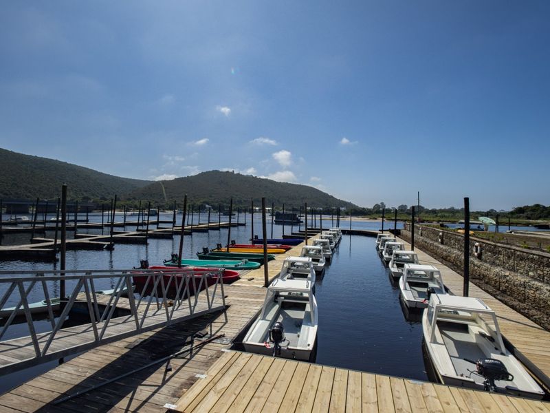 A scenic view of a private jetty and boat mooring area featuring wooden decking, a metal access ramp, and a stone retaining wall.