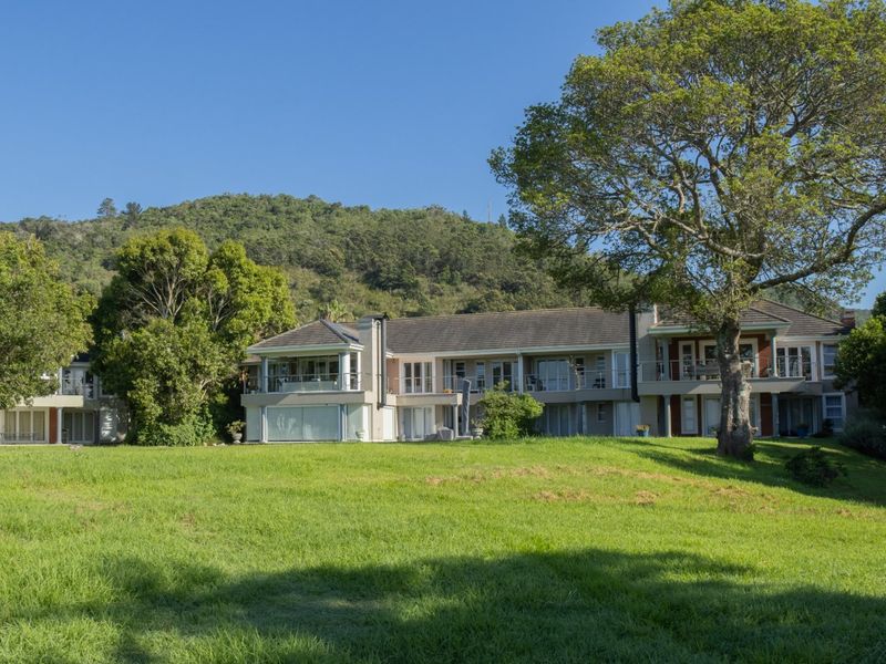 A rear view of the apartment complex featuring multiple balconies, sliding glass doors, and a spacious landscaped lawn set against a mountain backdrop.