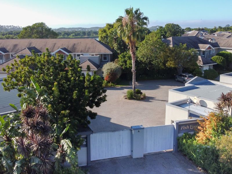 Aerial view of the residential complex entrance featuring a gated driveway, landscaped grounds, and multiple apartment buildings with tiled roofs.