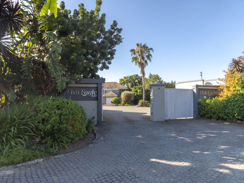 Entrance view of Fish Eagle Bay featuring a cobblestone driveway, gated access, and established garden landscaping leading towards the main property.