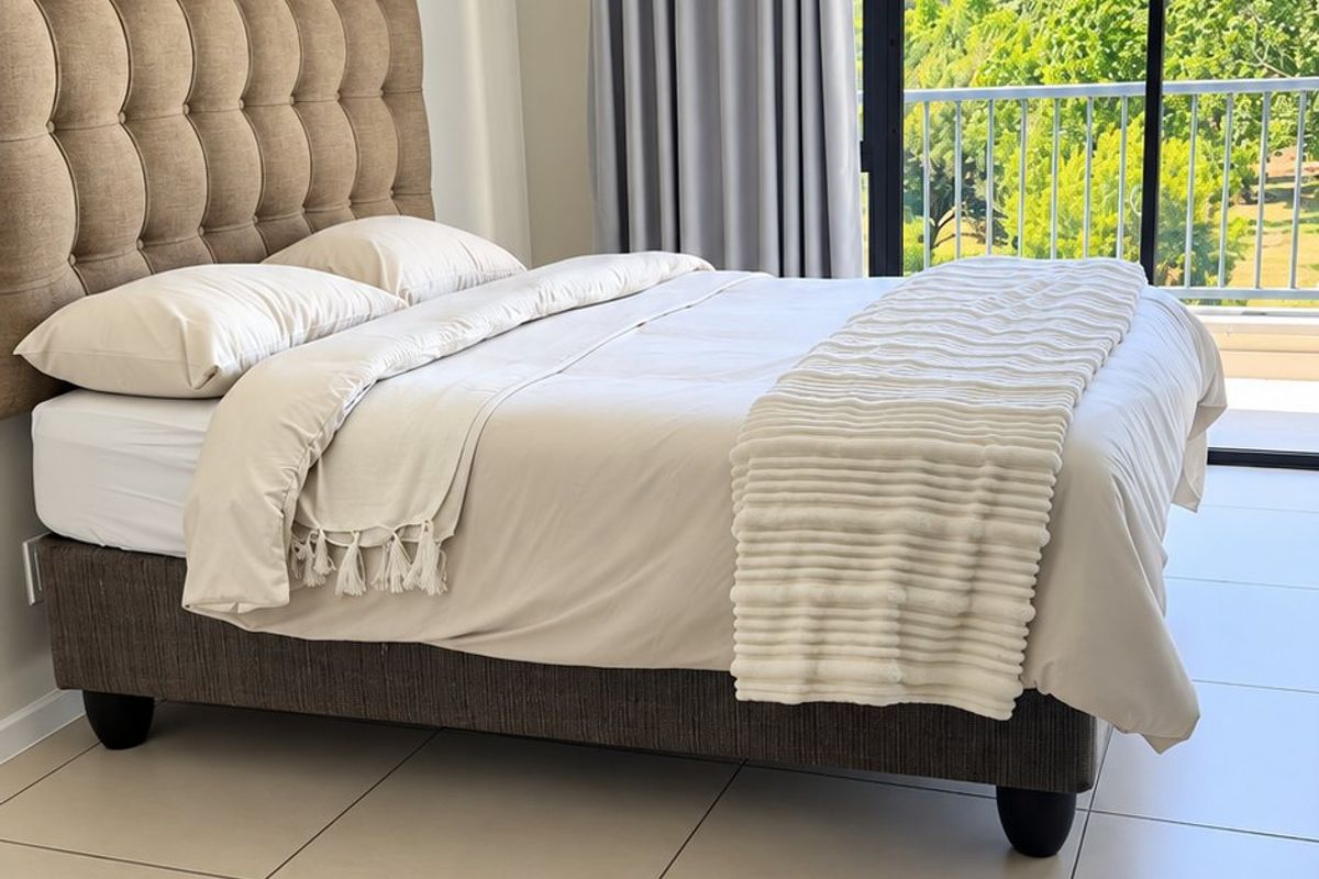 A bright bedroom featuring large format floor tiles, a coved ceiling, and a sliding glass door providing direct access to a private balcony.