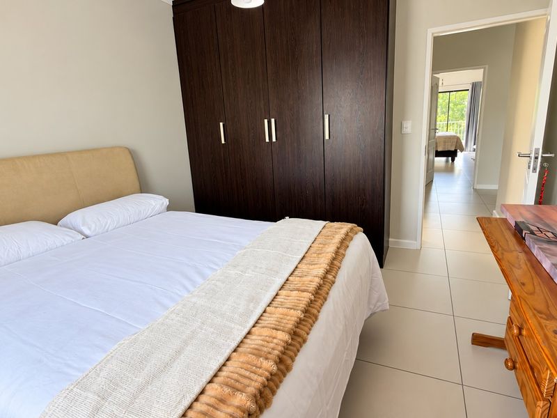 A well-maintained bedroom featuring dark wood built-in cupboards and neutral tiled flooring, with a view into the adjacent room.