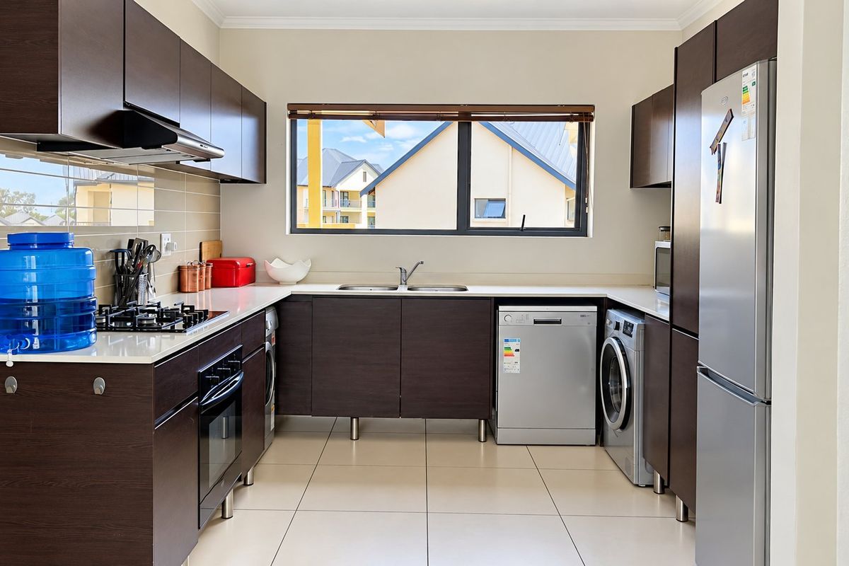 Modern kitchen featuring dark wood cabinetry, built-in oven, gas hob, extractor fan, and tiled flooring with a functional layout.
