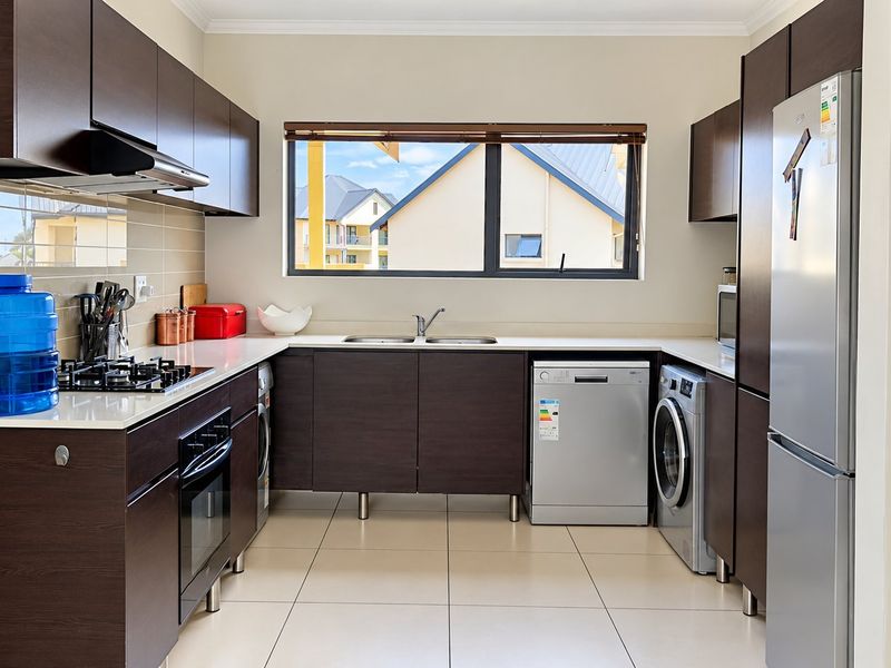 Modern kitchen featuring dark wood cabinetry, built-in oven, gas hob, extractor fan, and tiled flooring with a functional layout.