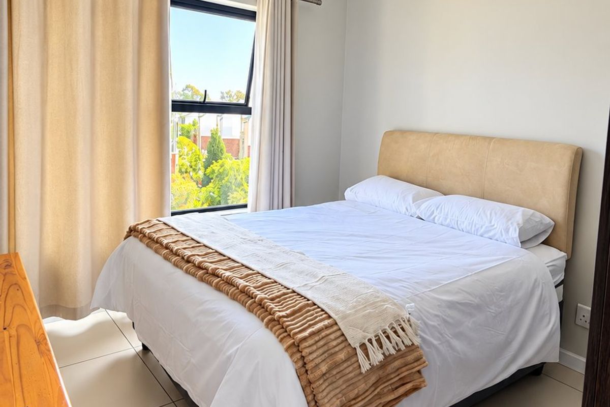 A bright and well-maintained bedroom featuring neutral tiled flooring, a modern pendant light, and a top-hung window with natural light.