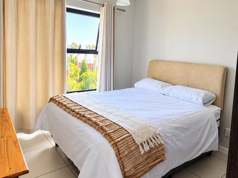 A bright and well-maintained bedroom featuring neutral tiled flooring, a modern pendant light, and a top-hung window with natural light.