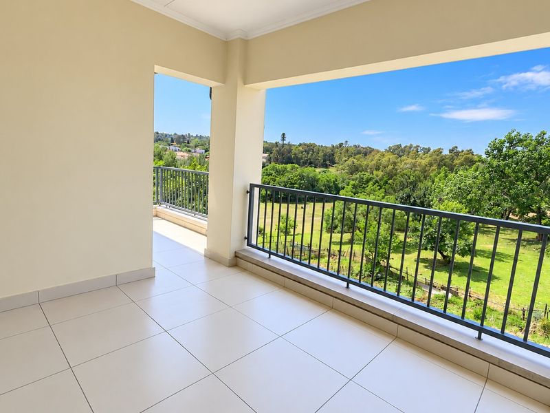A spacious covered balcony featuring tiled flooring and a metal balustrade, offering scenic views of the surrounding greenery.