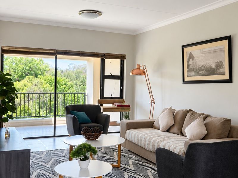 A bright and well-maintained living room featuring neutral tiled flooring and direct access to a private balcony through large sliding glass doors.