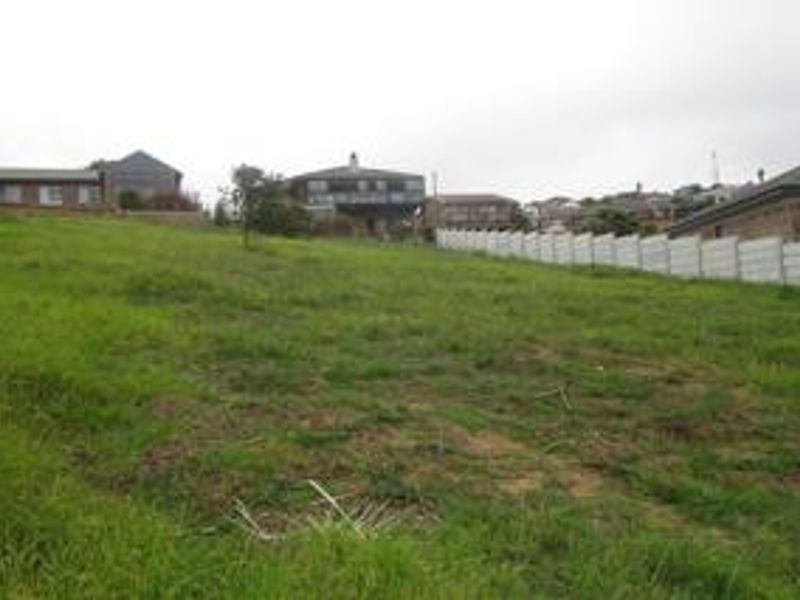 A vacant residential plot of land featuring a grassy surface and a precast concrete boundary wall, situated in a developed neighborhood.