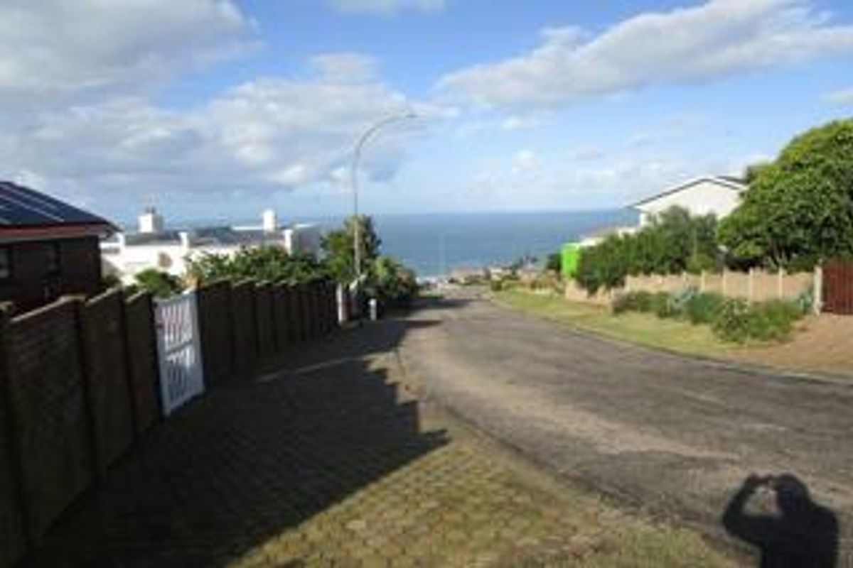A street view looking down a paved residential road towards the ocean, featuring brick boundary walls and established neighborhood infrastructure.