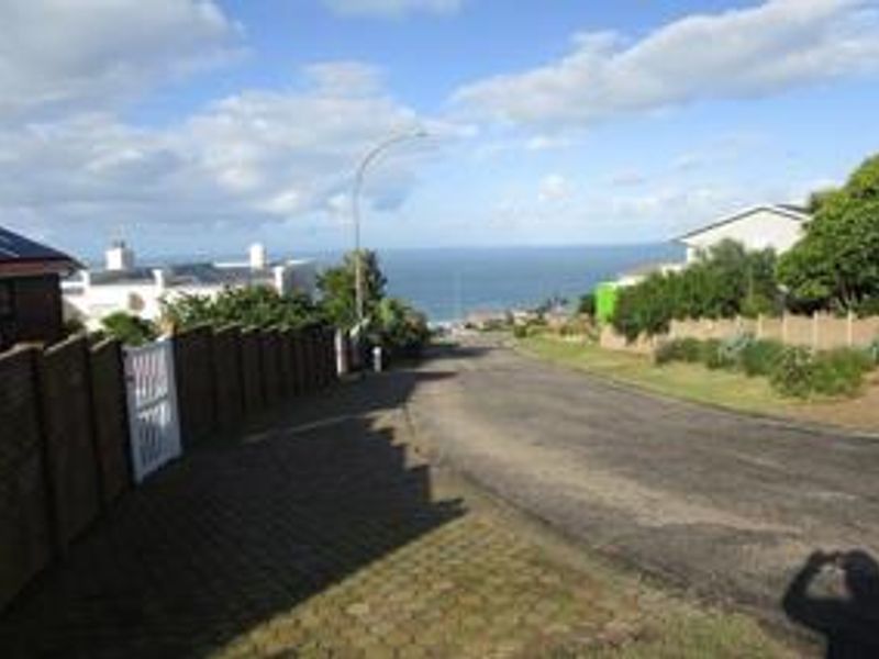 A street view looking down a paved residential road towards the ocean, featuring brick boundary walls and established neighborhood infrastructure.