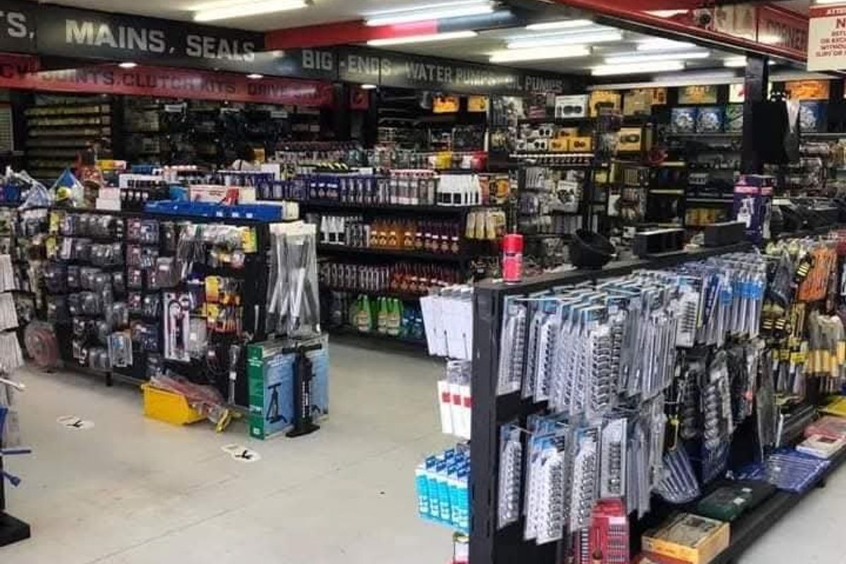 A commercial retail space featuring exposed structural steel beams, industrial fluorescent lighting, and durable concrete flooring, currently utilized for automotive parts display.
