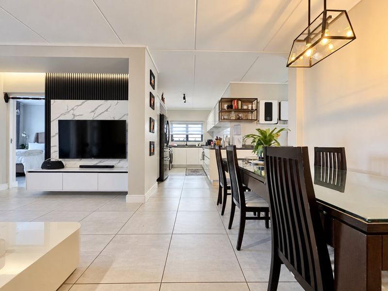 Modern open-plan living and dining area featuring a sleek media wall, tiled floors, and a contemporary kitchen with clean lines and integrated cabinetry.