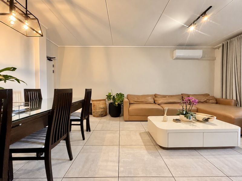 Spacious open-plan living and dining area featuring neutral tiled flooring, modern lighting fixtures, and a wall-mounted air conditioning unit.