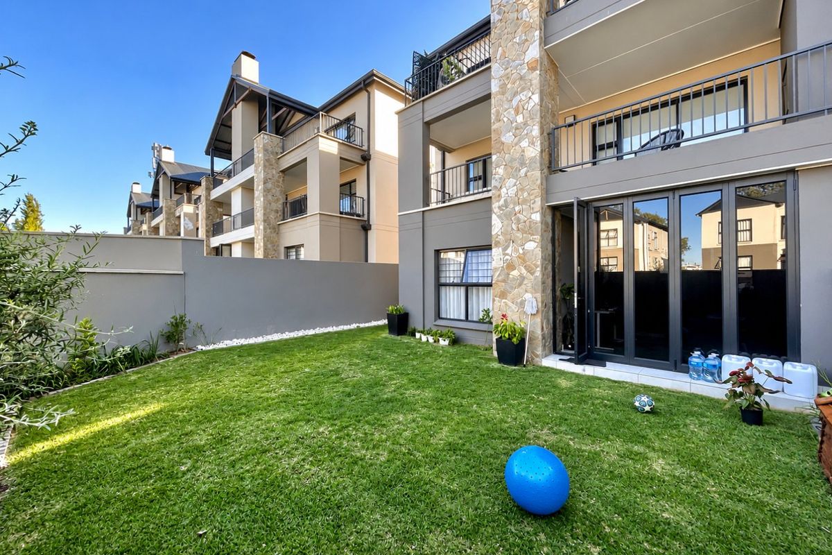 A well-maintained rear garden featuring a manicured lawn, stone-clad pillars, and modern bi-fold doors leading to the townhouse interior.