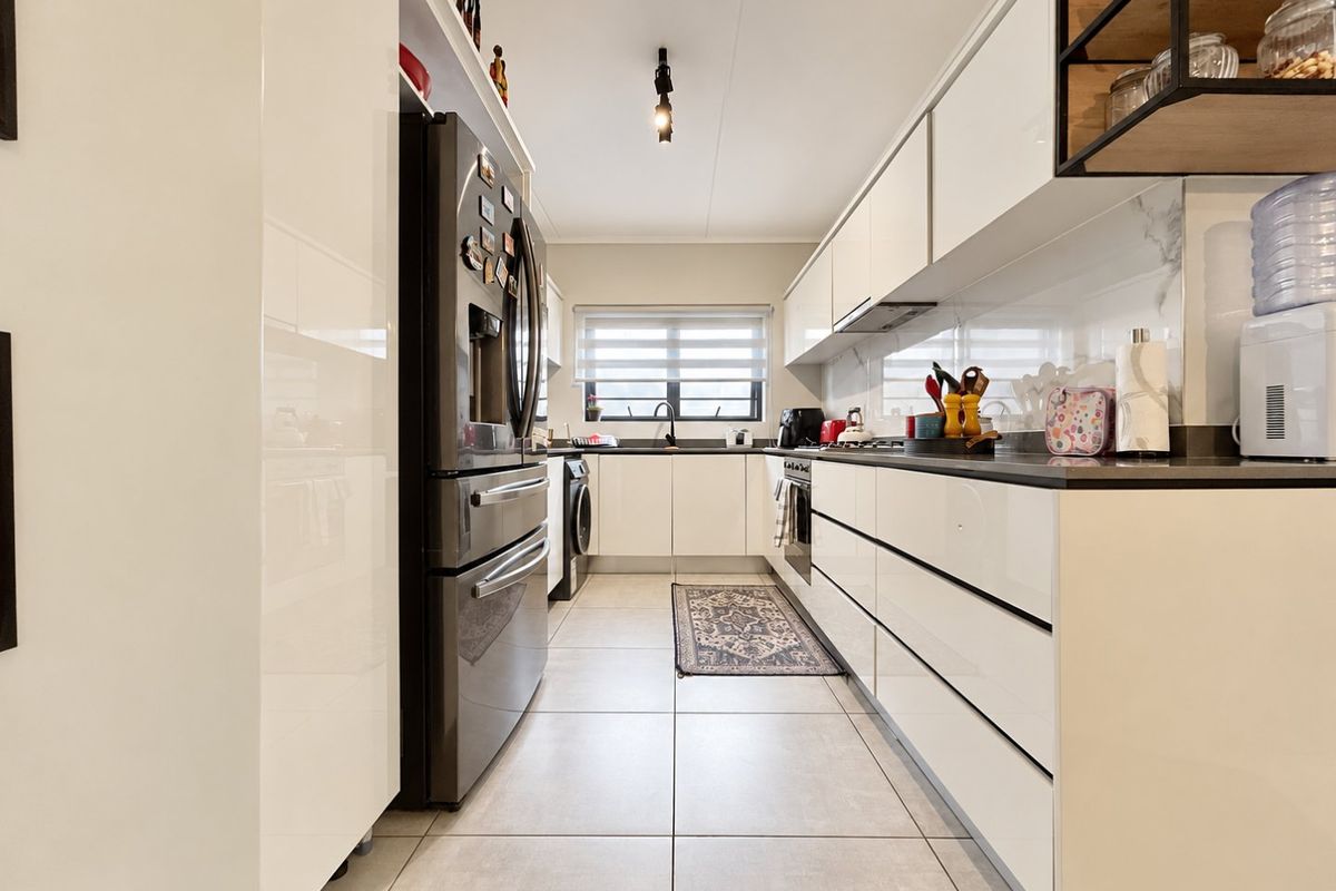 Modern galley-style kitchen featuring high-gloss white cabinetry, stone countertops, integrated appliances, and large format floor tiles.