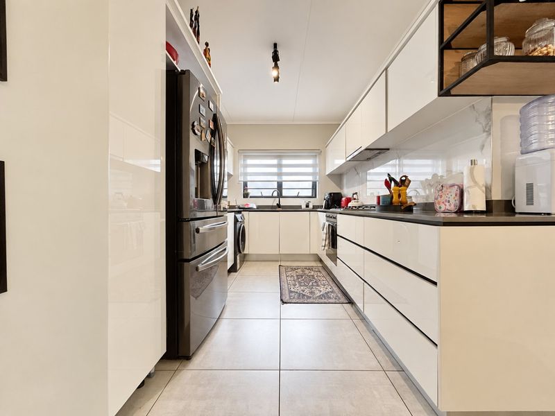 Modern galley-style kitchen featuring high-gloss white cabinetry, stone countertops, integrated appliances, and large format floor tiles.