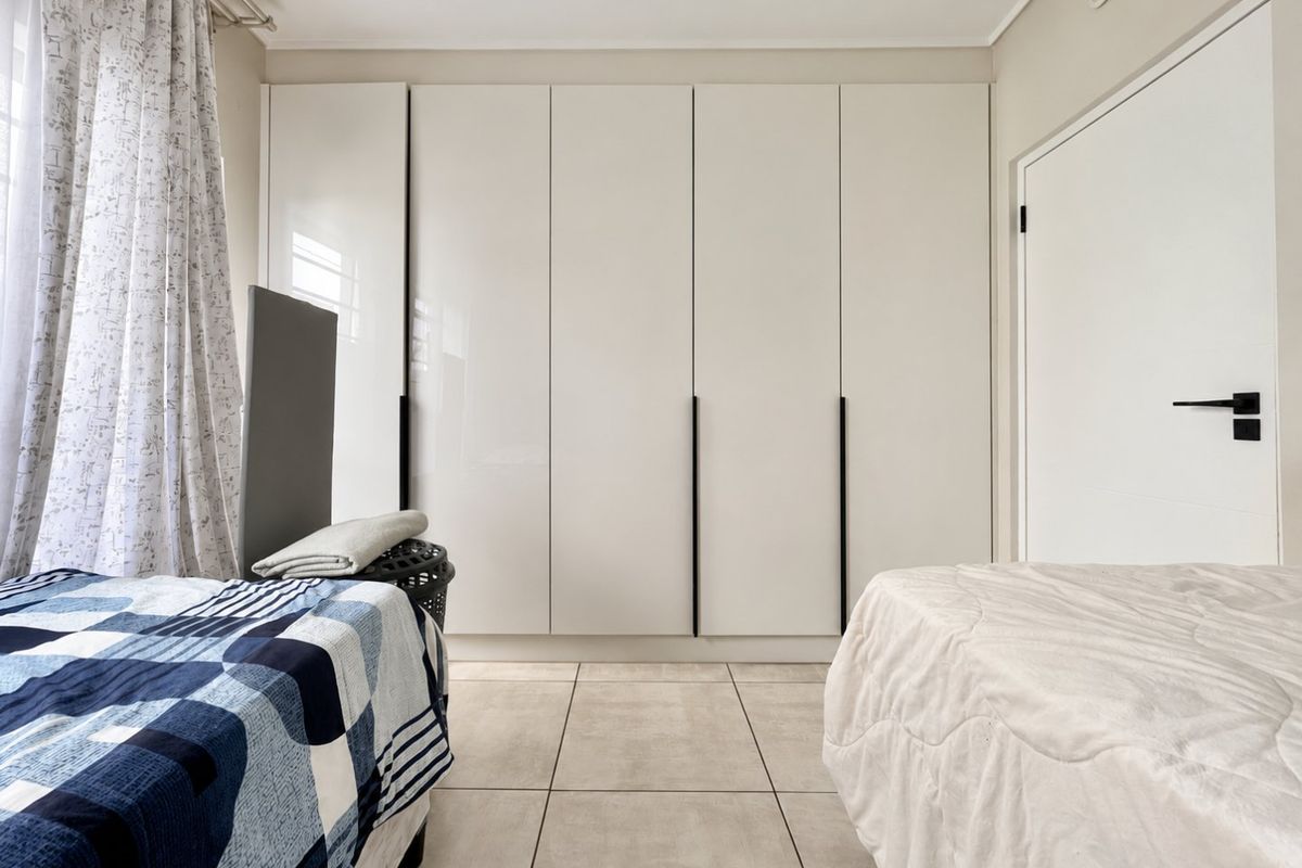 A well-maintained bedroom featuring modern floor-to-ceiling built-in cupboards with sleek black handles and neutral tiled flooring.