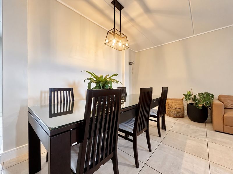 A bright dining area featuring neutral walls, large format floor tiles, and a modern geometric pendant light fixture.