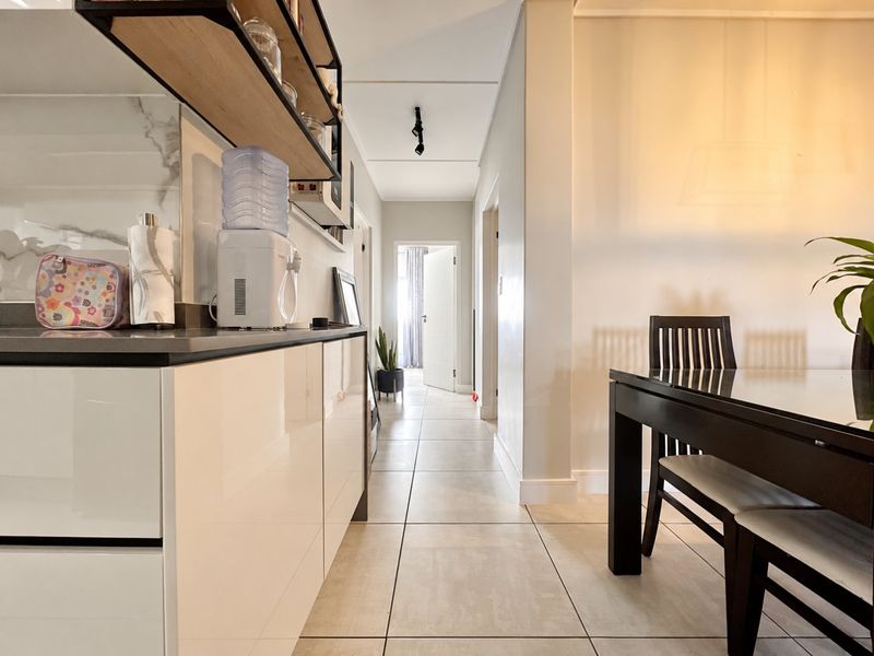 Modern open-plan kitchen and dining area featuring high-gloss cabinetry, stone countertops, marble-look splashback, and neutral tiled flooring throughout.