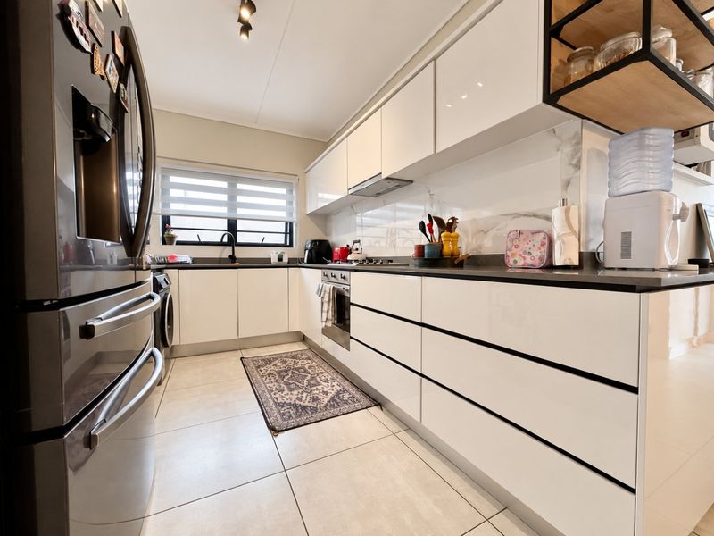 Modern kitchen featuring sleek white cabinetry, stone countertops, integrated appliances, and tiled flooring, offering a clean and functional culinary space.