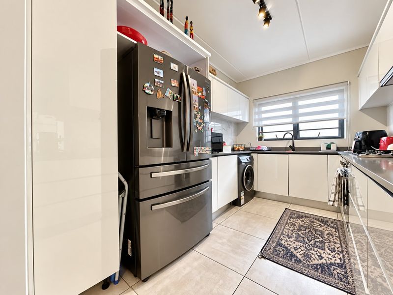 Modern kitchen featuring sleek white cabinetry, tiled flooring, integrated laundry appliances, and a functional layout with ample counter space and natural light.