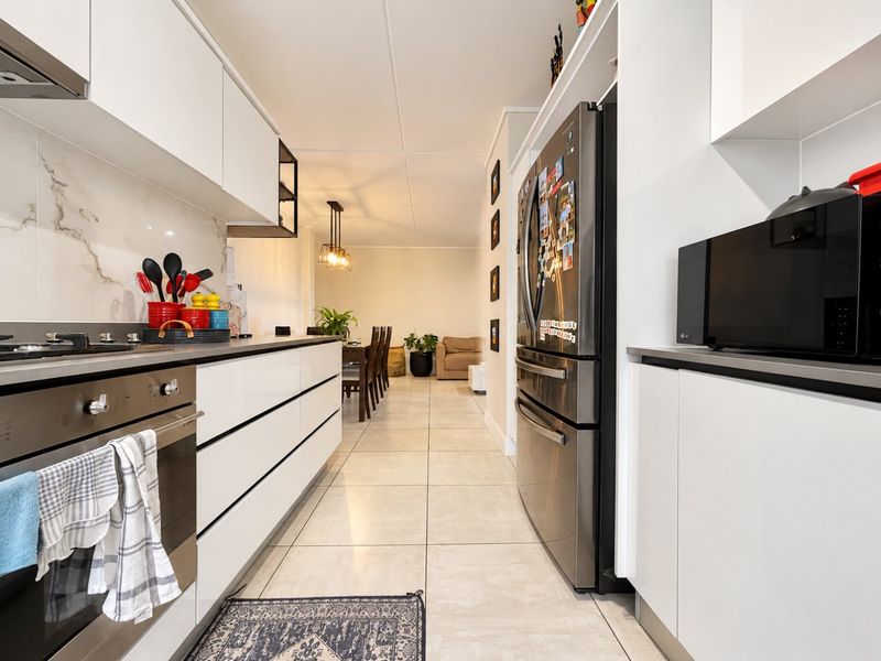 Modern open-plan kitchen featuring sleek white cabinetry, integrated appliances, and marble-look splashback, flowing seamlessly into the dining and living area.