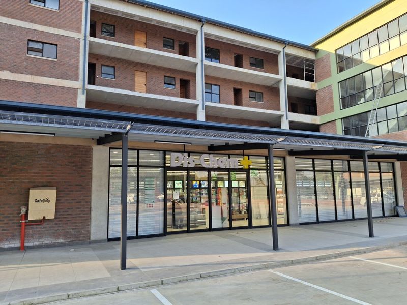 Exterior view of a modern apartment building with a ground-floor commercial storefront and covered pedestrian walkway.