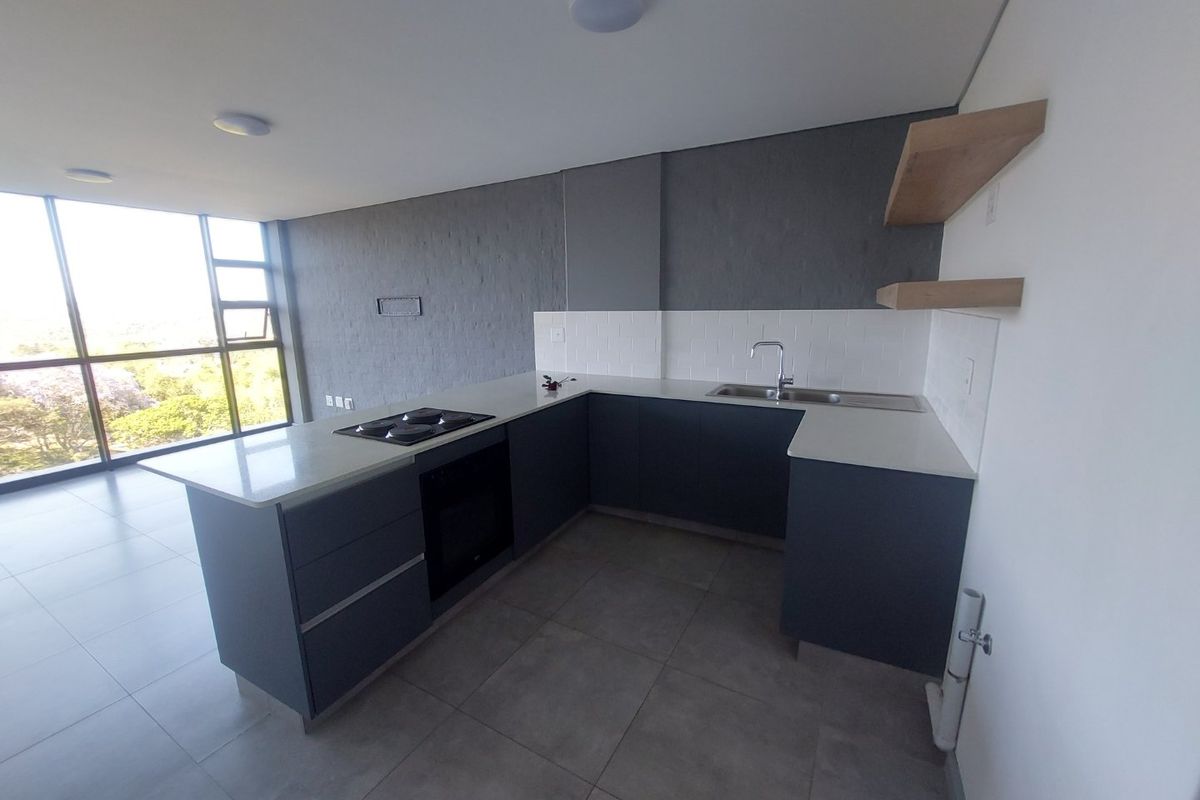 Modern open-plan kitchen featuring dark cabinetry, quartz countertops, built-in oven, electric hob, and large windows offering natural light and scenic views.