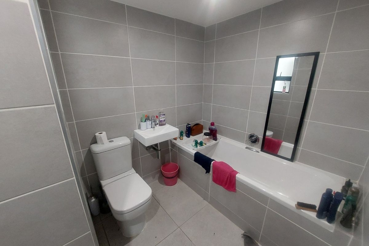A modern bathroom featuring grey ceramic wall and floor tiles, a wall-mounted basin, a standard toilet, and a built-in bathtub.