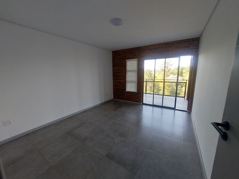 A bright, empty bedroom featuring modern grey floor tiles, an exposed brick feature wall, and sliding glass doors leading to a private balcony.