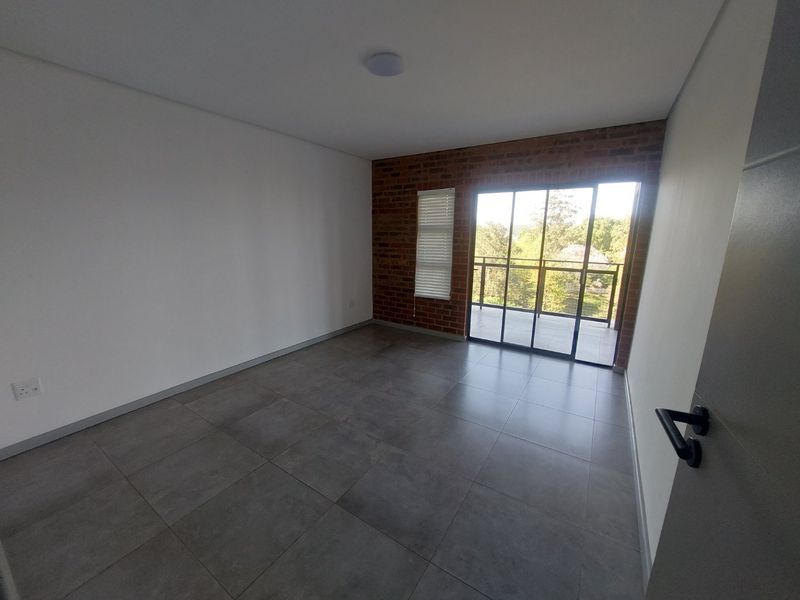 An empty bedroom featuring modern tiled flooring, an exposed brick feature wall, and a sliding glass door providing access to a private balcony.
