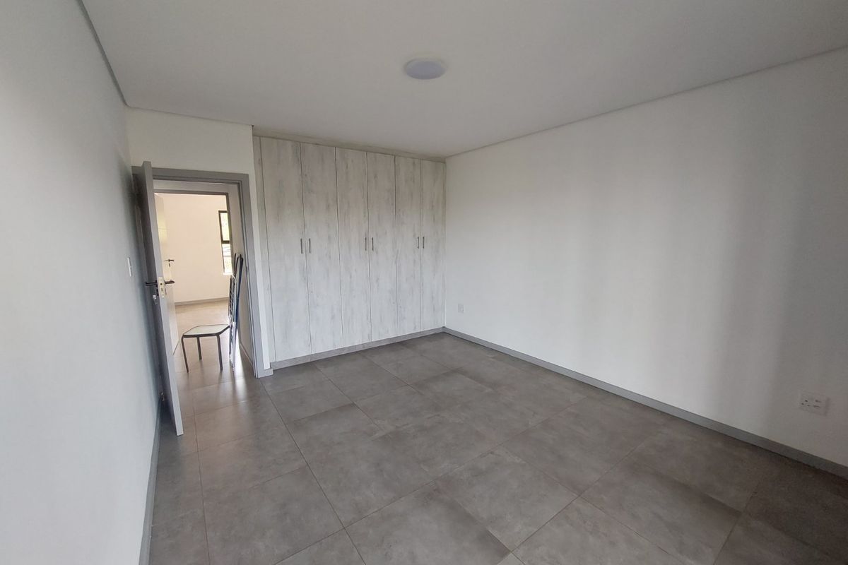 A clean, modern bedroom featuring neutral tiled flooring and ample built-in cupboard storage, offering a bright and versatile living space.
