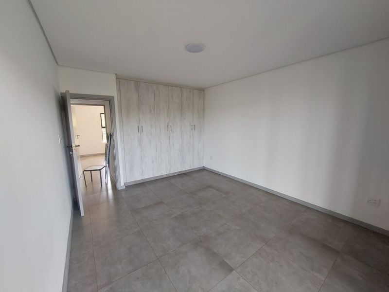 A clean, modern bedroom featuring neutral tiled flooring and ample built-in cupboard storage, offering a bright and versatile living space.