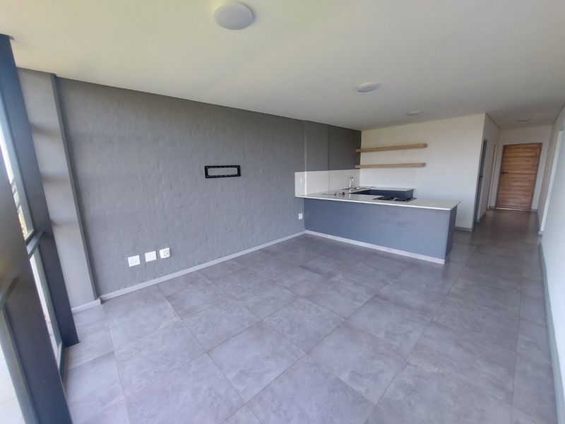 Modern open-plan living area featuring a sleek kitchen with a central island, hob, and contemporary grey tiled flooring throughout.