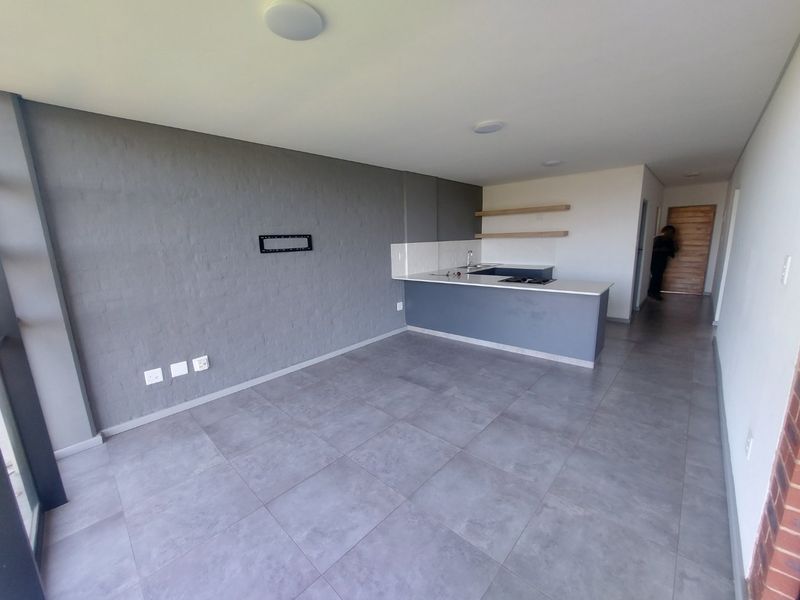 Modern open-plan living area featuring a sleek kitchen island with built-in hob, tiled flooring, and neutral grey accent wall.